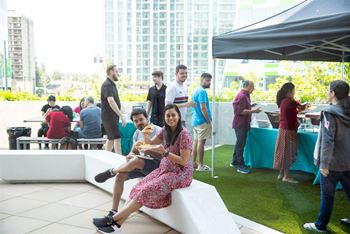 A woman in a floral dress is sitting on a bench eating while surrounded by people.